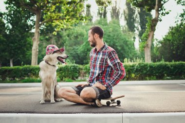 Kaykay ile komik Sibirya husky köpek şapkalı üzerinde oturan genç hipster adam 