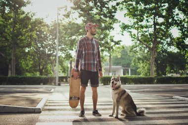 Sokak yol üzerinde kaykay ve Sibirya husky köpek duran adamla genç yenilikçi