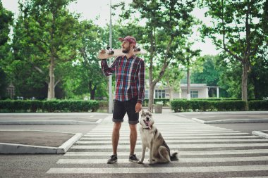Sokak yol üzerinde kaykay ve Sibirya husky köpek duran adamla genç yenilikçi