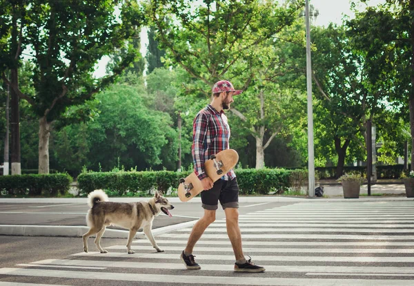 Kaykay ve Sibirya husky köpek ile sokak yolda yürüyen genç hipster adam