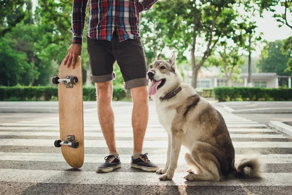 Close up de homem com skate e siberiano cão husky na estrada de rua — Fotografia de Stock