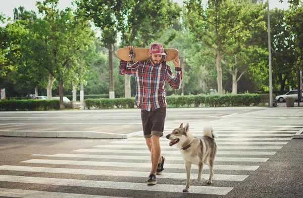 Joven hipster hombre caminando con monopatín y perro husky siberiano en la calle carretera — Foto de Stock