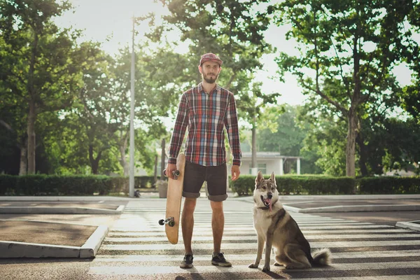Sokak yol üzerinde kaykay ve Sibirya husky köpek duran adamla genç yenilikçi