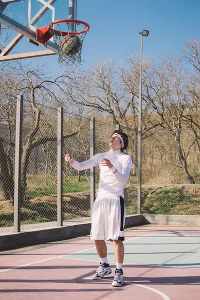 Retrato de um jogador de basquete andando em um campo de basquete ao ar livre e driblando a bola — Fotografia de Stock