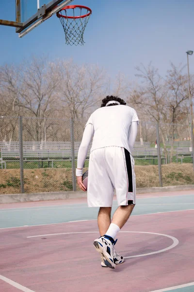 Retrato de um jogador de basquete andando em um campo de basquete ao ar livre e driblando a bola — Fotografia de Stock