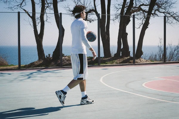 Retrato de um jogador de basquete andando em um campo de basquete ao ar livre e driblando a bola — Fotografia de Stock