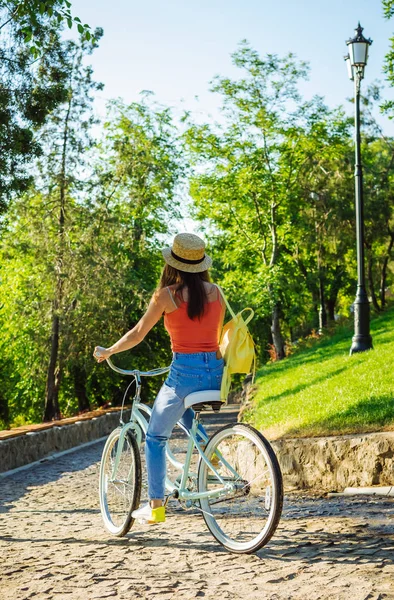 Genç güzel kadın yaz Park'taki bisiklet sürme. Yeşil ağaçlar arka plan 