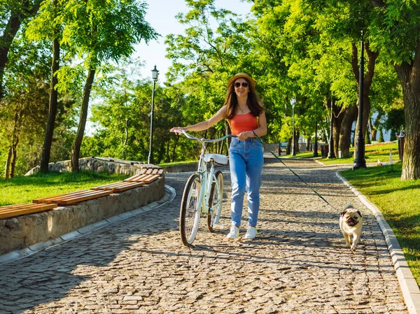 Genç güzel kadın vintage Bisiklet ve yaz Park'ta yürüyordunuz pug. Yeşil ağaçlar arka plan    