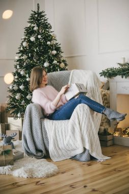 Koltukta oturan ve Noel açma genç güzel kadın sunmak, kapalı