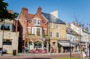 Tynemouth tarihi şehir merkezinde bir açık bahar gününde kafeler ve barlar dışında masalarda oturan insanlar