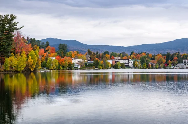 Edifici e alberi autunnali colorati che si riflettono nelle acque calme di un lago di montagna — Foto Stock