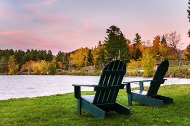 Boş Adirondack sandalyeler çimenlerin üzerinde bir gölün kıyısında gece karanlığında yakınındaki.