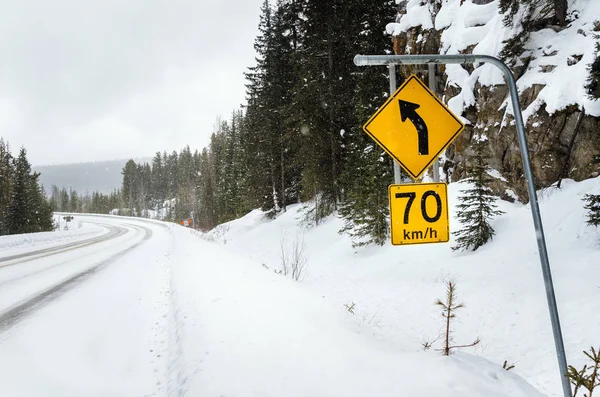 Знак ограничения скорости перед опасным поворотом вдоль снежной дороги — стоковое фото