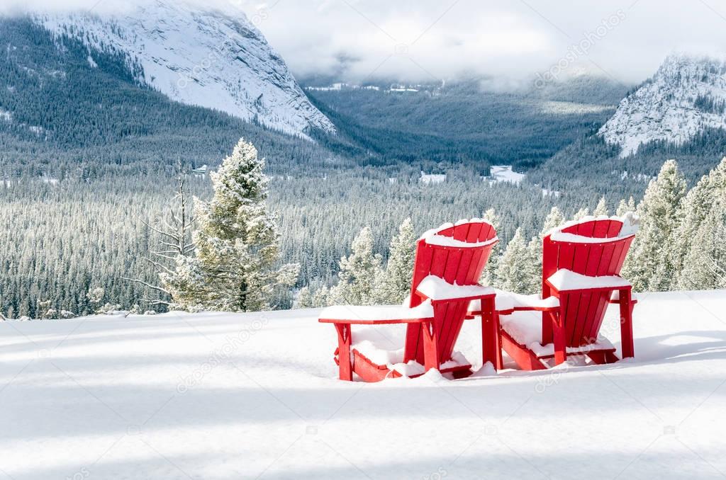 Two Red Adirondack Chairs Facing a Snowy Mountain Landscape