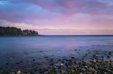Deniz taşlar ön planda ve arka planda bir güneşli dağ öfke alacakaranlıkta manzarası