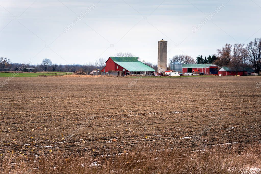 Ploughed Field with a Farm with Grain Bins in Background on a Cloudy Winter Day. Ontario, Canada.