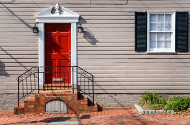 Front of a Traditional Wooden House with a Red Door, White Window with Black Shutters, and Red Brick Steps on a Sunny Autumn Morning. Alexandria, VA. clipart