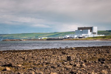 Sahilde, bulutlu bir bahar gününde arka planda ekili tepeleri olan bir nükleer santralin fotoğrafı. Dunbar, İskoçya, Uk.