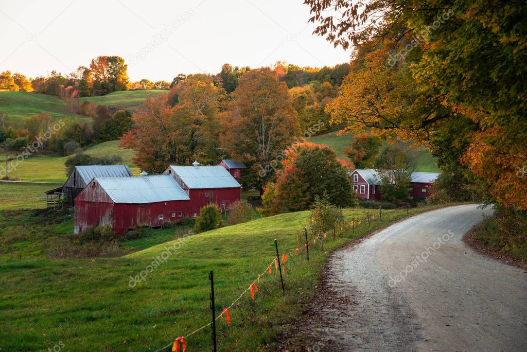 Traditional American farm with a red wooden barn in a rolling rural landscape in autumn. Beautiful fll colors. Woodstock, VT, USA.