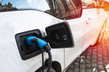 Şehir merkezindeki kaldırımlı bir cadde boyunca park halindeyken şarj edilen elektrikli bir arabaya takılan güç kaynağını kapatın. Brüksel, Belçika.