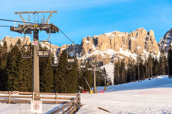 晴れた冬の日にドロマイトの岩場のピークのふもとに雪のスキー場の上に空の椅子リフト — ストック写真