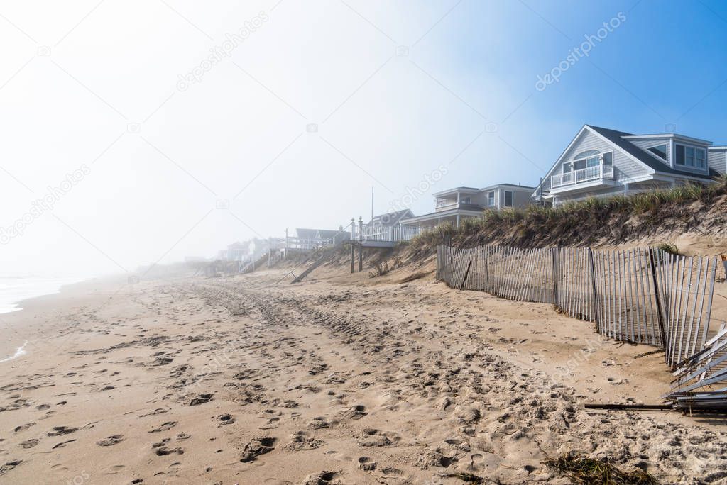 Deserted sandy beach lined with holiday houses and wooden fences on a foggy autumn morning. Seabrook, NH, USA.