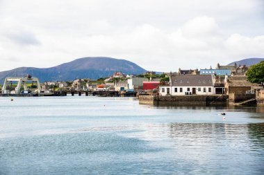 Bulutlu bir bahar gününde arka planında bir dağ olan güzel bir sahil köyü. Stromness, Orkney Adaları, İskoçya, Uk.
