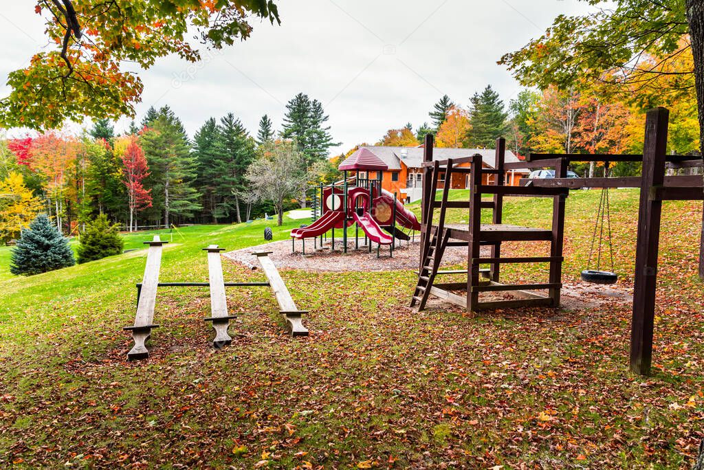 Deserted children playground in a public park surrounded by colourful autumnal trees on a cloudy morning. Vermont, USA.