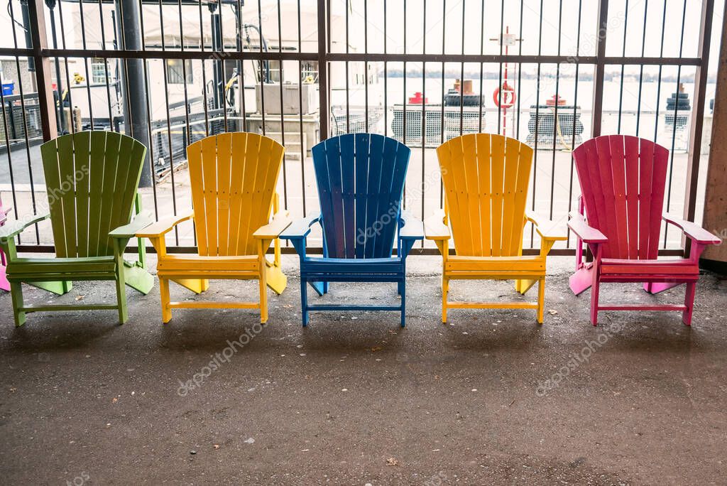 Row of empty colourful adirondack chairs against a metal fence. Toronto, ON, Canada.