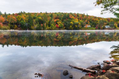 Sonbahar mevsiminde orman kıyıları boyunca yazlık evleri olan güzel dağ gölü. Vermont, ABD.