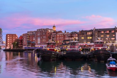 Günbatımında Portsmouth ufuk çizgisi ve rıhtım manzarası. Üç demirli römorkör ön planda. NH, ABD.