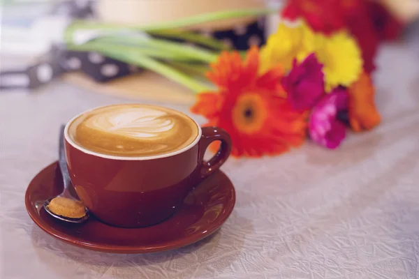 Una taza de café con arte en una mesa, flores borrosas en el fondo — Foto de Stock