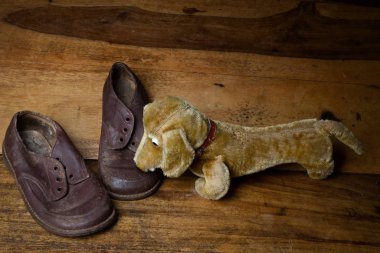 Old children shoes and a toy dog on wooden floor clipart