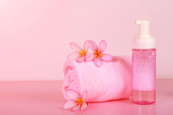 Spa composition with towel, flowers and bottle of soap on pink background