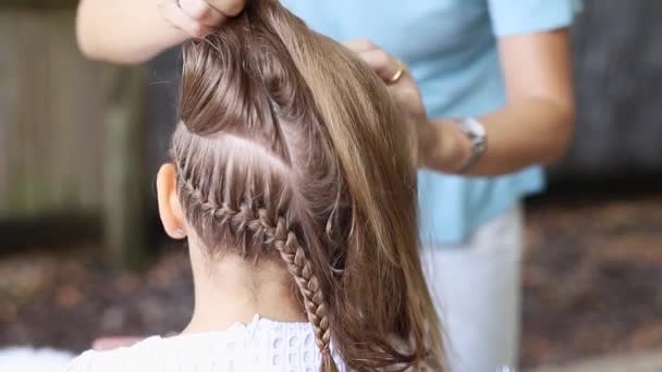 Mère tresse ses filles de longs cheveux blonds. Des mains de femmes blanches. et petite fille en robe blanche . — Video