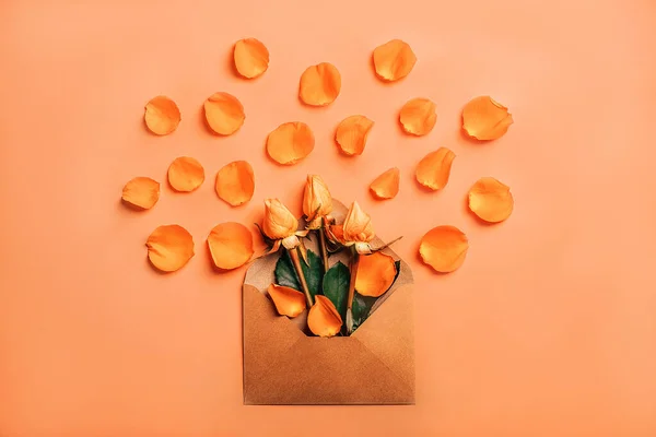 Sobre de papel artesanal con rosas naranjas en pétalos sobre fondo coral — Foto de Stock