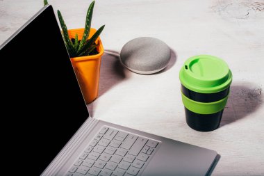 Bilgisayarlı akıllı hoparlör, portakal kabında aloe vera bitkisi ve beyaz arka planda yeşil kapaklı yeniden kullanılabilir kahve fincanı..