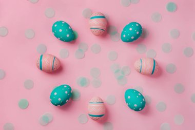 Pink and mint colored decorated eggs on pink background with confetti.