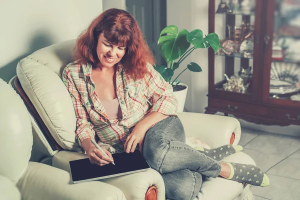 Mujer de mediana edad feliz trabajando en casa en un portátil sentado en la cama en la casa . — Foto de Stock