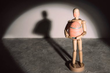 Maskeli ahşap kukla hedeflenmiş ışıkta renkli yumurta tutuyor..