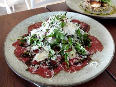 Et carpaccio tabağı taze yeşil salata ve beyaz tabakta hindistan cevizi gevreği ile servis edilir.