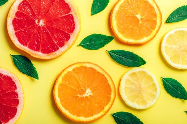 Turuncu, limon, greyfurt dilimleri ve sarı arka planda naneli otlar..