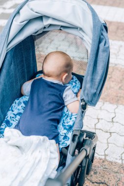 Bebek arabasındaki küçük bebek karnının üstünde yatar ve pencereden dışarı bakar.