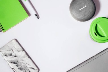Akıllı hoparlörlerin düz yatışı, öncü ışıklar kırpılmış akıllı telefon, yeşil not defteri, kalem ve yeniden kullanılabilir kahve fincanı ile etkinleştirildi.