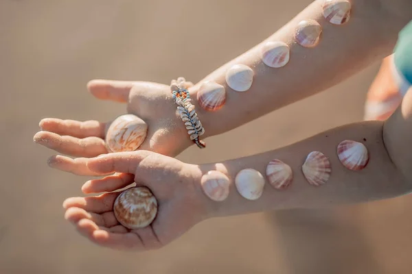 Маленькие девочки руки с ракушками на них на фоне океана песчаный пляж . — стоковое фото