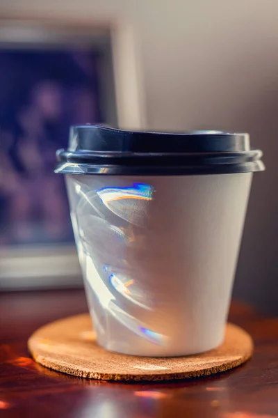 Una taza de café para llevar en el escritorio con marco de fotos borrosas en el fondo — Foto de Stock
