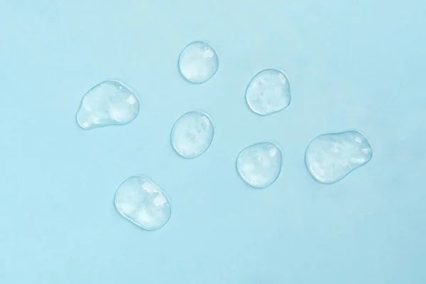 Squeezed cosmetic clear cream gel texture. Close up photo of transparent drop of skin care product. High Quality transparent gel with bubbles closeup on blue background — Stock Photo, Image