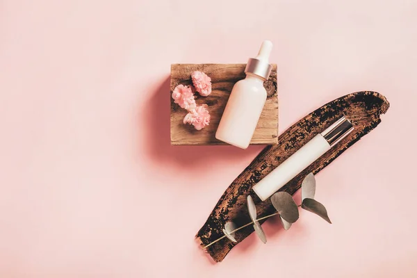 Botol kosmetik pada batang kayu dengan eukaliptus dan bunga begonia pada latar belakang kertas merah muda — Stok Foto