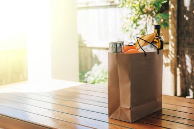 Bir evin arka bahçesindeki ahşap masada içinde yiyecek olan kağıt torba..