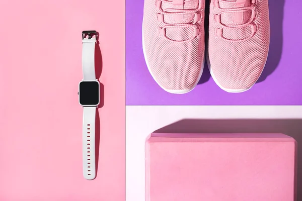 New pink sneakers, yoga block and smart watch on colorful background. Overhead shot of running shoes.